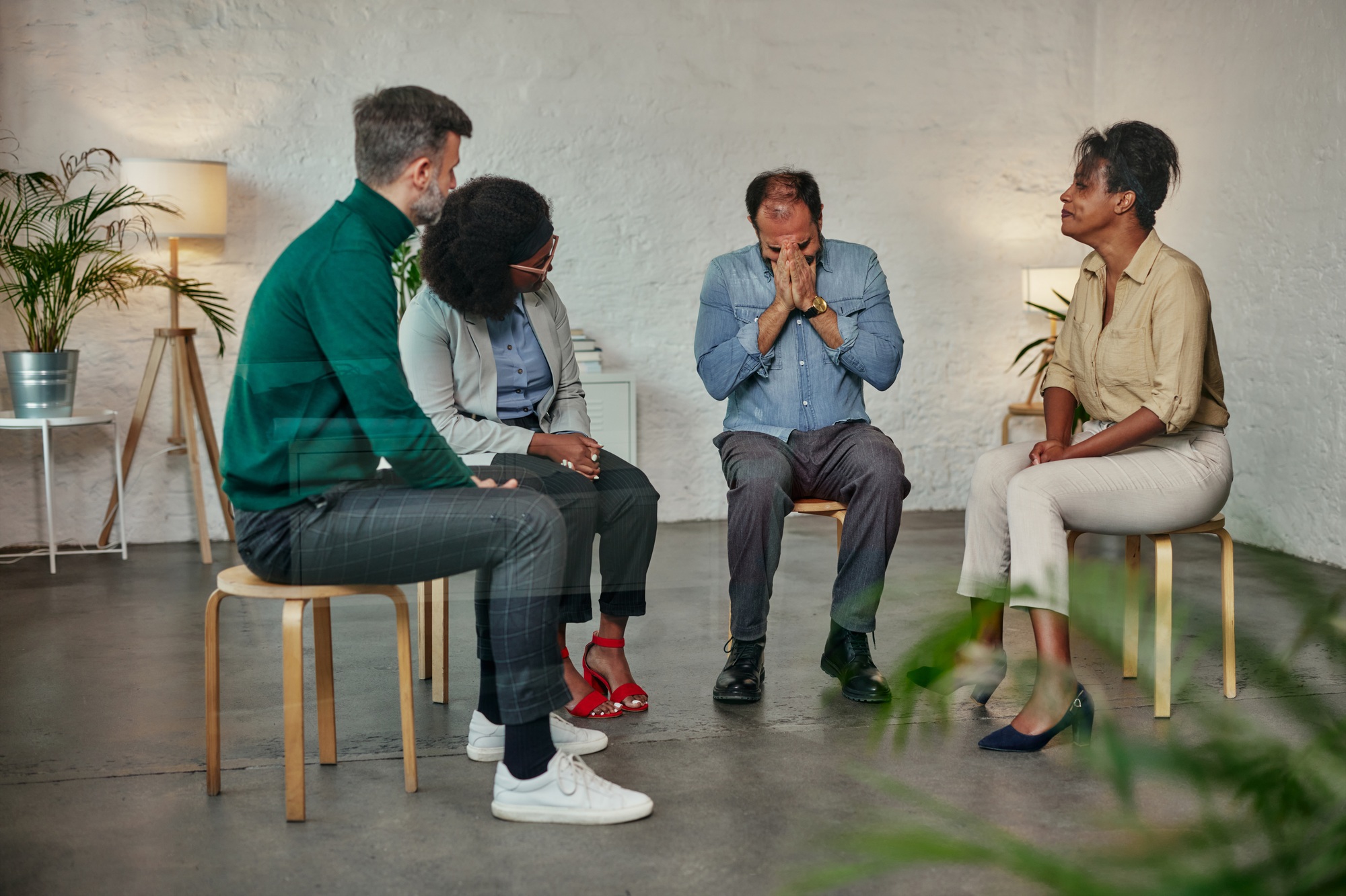 Group therapy session members supporting crying desperate man