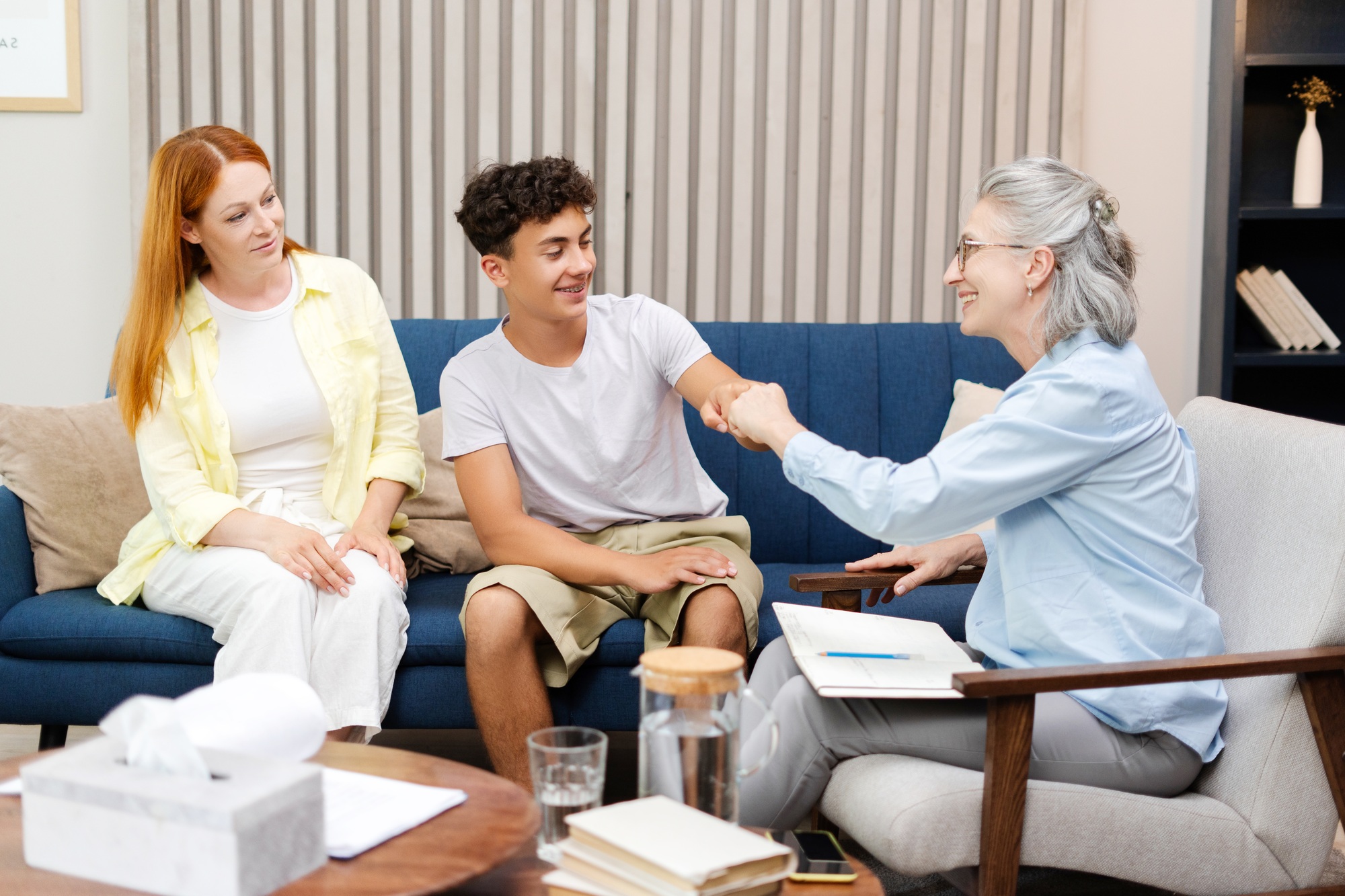 Happy teenage boy giving fist bump with therapist after successful therapy session